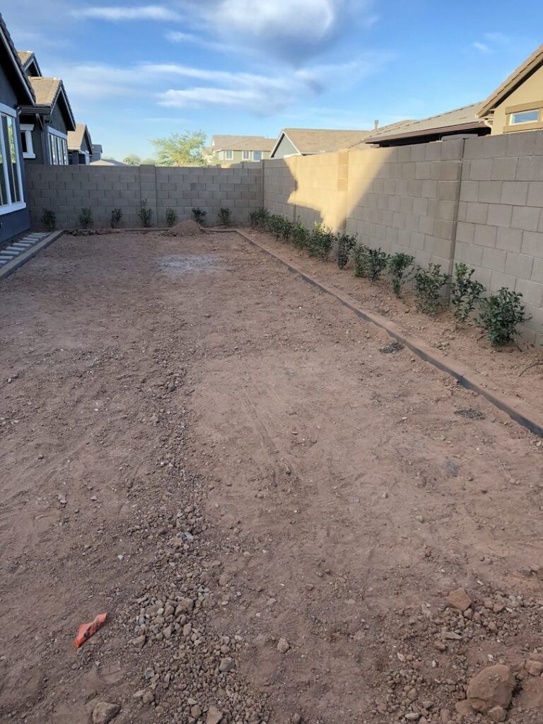 Desert landscape installation area in Phoenix, AZ, featuring bare soil, outlined planting beds, and newly planted shrubs against a block wall, showcasing potential for landscaping services by Core Landscape.