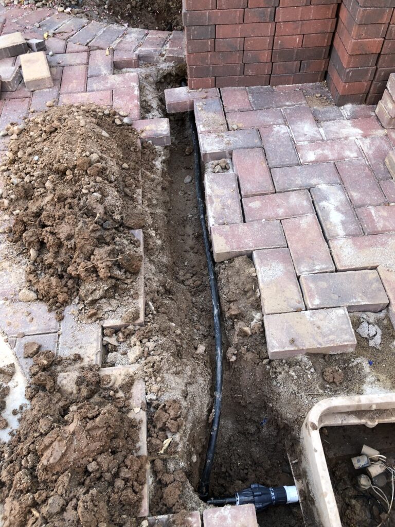 Drip irrigation system installation in progress, showcasing a trench with black irrigation tubing and surrounding paver bricks, emphasizing Core Landscape's irrigation services in Phoenix, AZ.