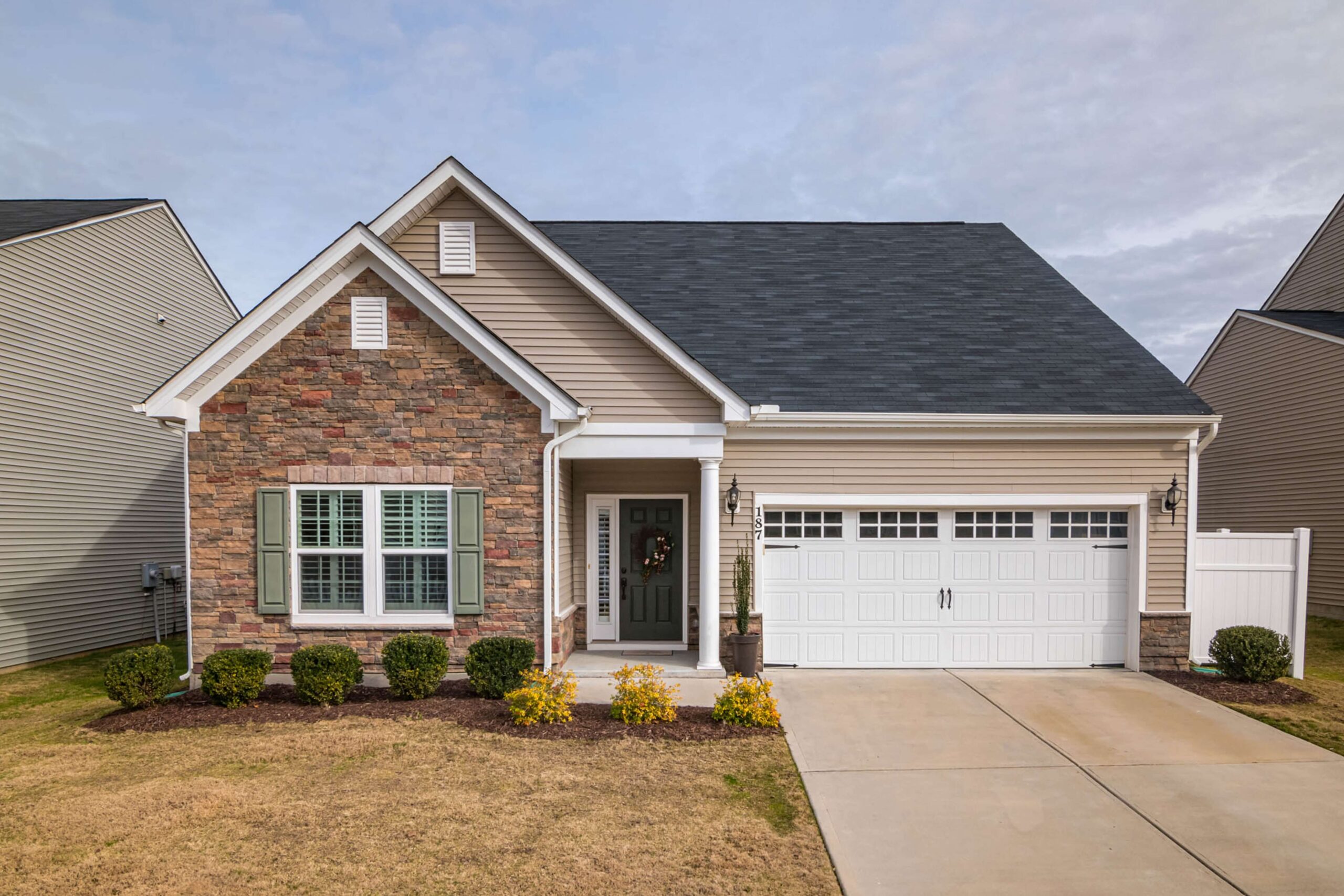 Front view of a well-maintained home featuring stone and vinyl siding, manicured shrubs, and yellow flowering plants, illustrating enhanced curb appeal for increased property value.