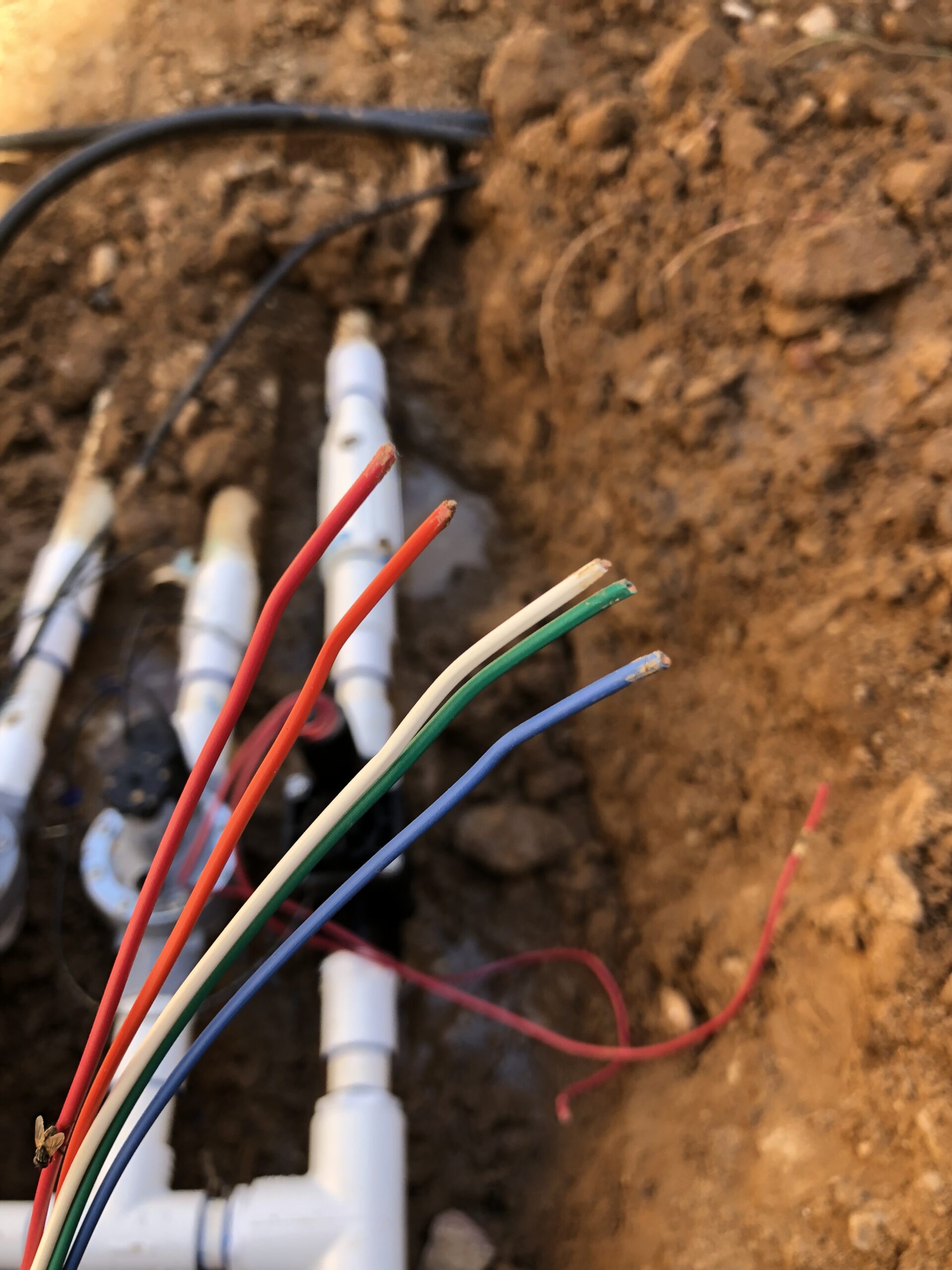Irrigation wiring with colored electrical wires in a trench near irrigation valves and pipes, representing professional electrical services for irrigation systems in Phoenix, AZ.