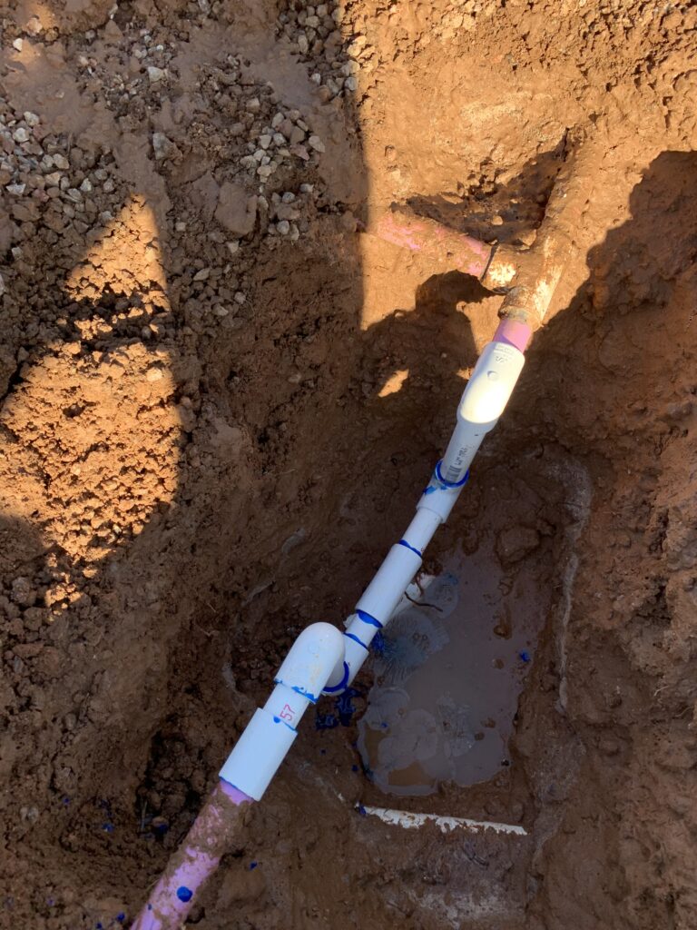 Mainline pipe installation in a trench, showcasing PVC pipes and surrounding soil, relevant to Core Landscape's irrigation repair services in Phoenix, AZ.