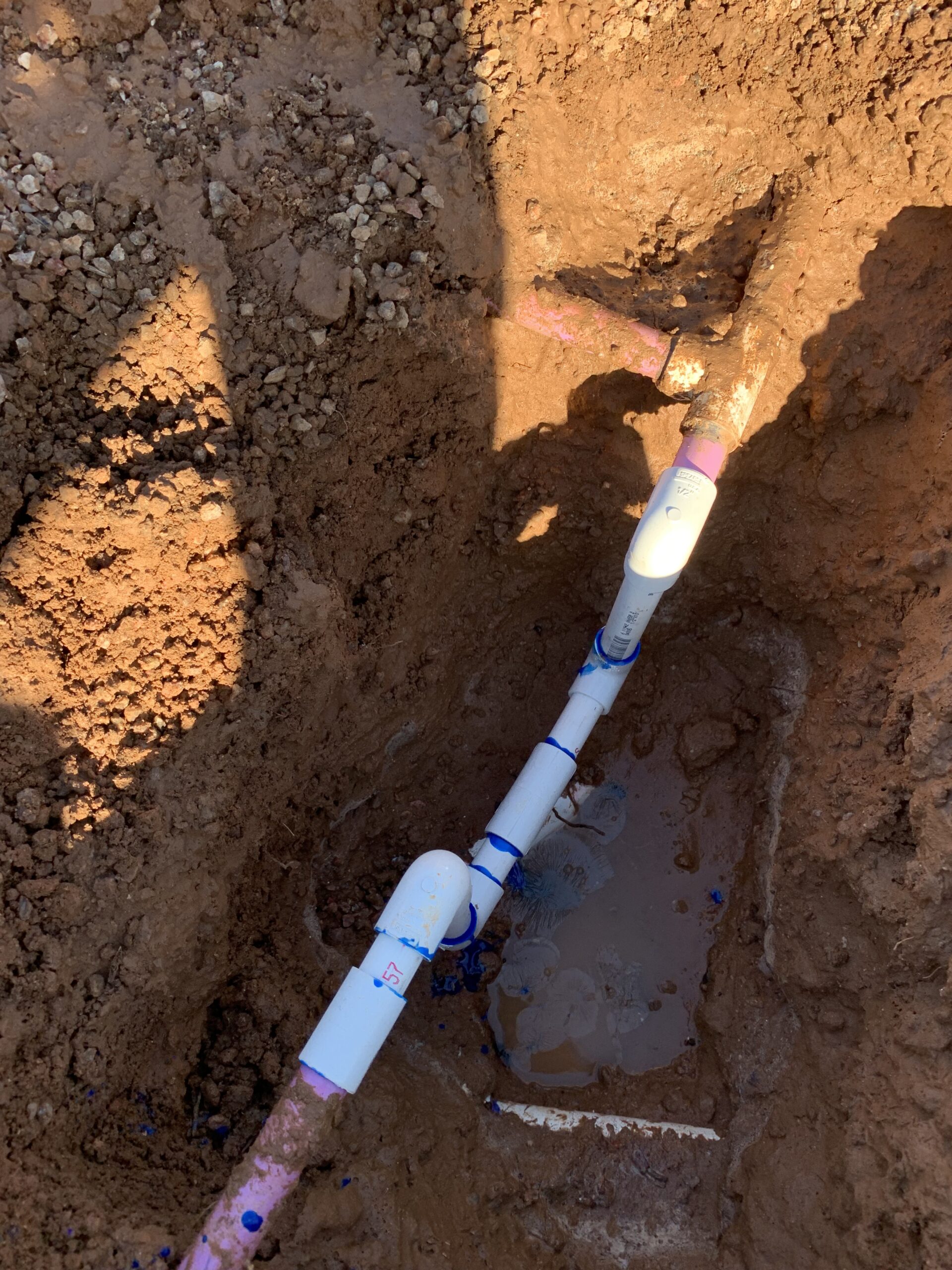 Mainline irrigation pipes in a trench, showing repair work with visible water pooling, emphasizing Core Landscape's mainline pipe repair services in Phoenix, AZ.