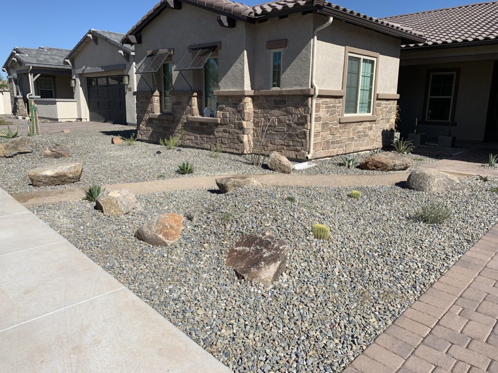 Energy-efficient desert landscaping featuring rocks and low-water plants in front of a residential home in Phoenix, AZ.