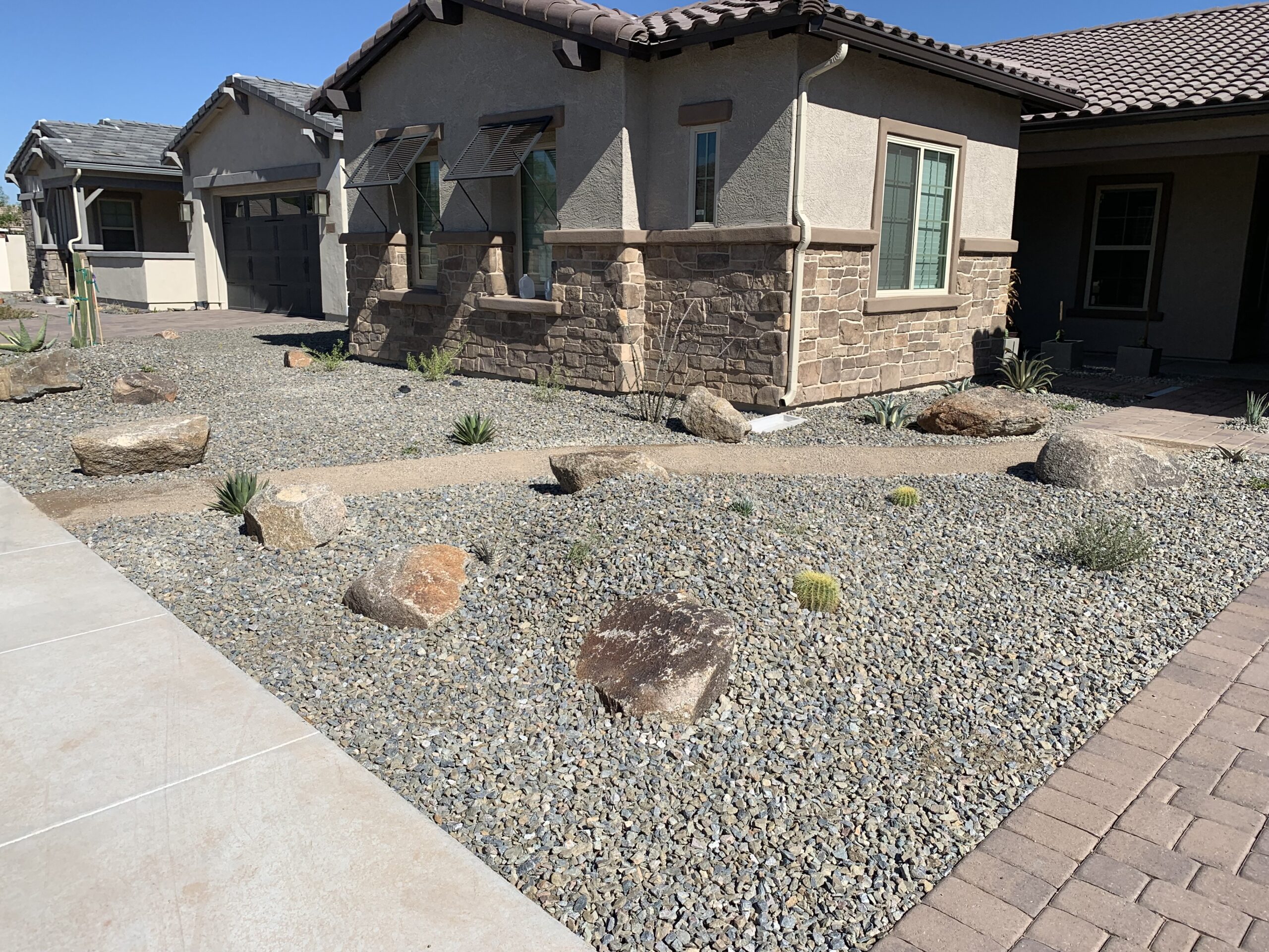 Energy-efficient landscaping featuring desert plants and boulders in a residential Arizona front yard, designed for minimal water use and cooling benefits.