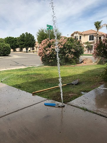 Water line leak spraying upward from the ground with tools nearby, illustrating a sprinkler system issue in a residential area of Phoenix, AZ.
